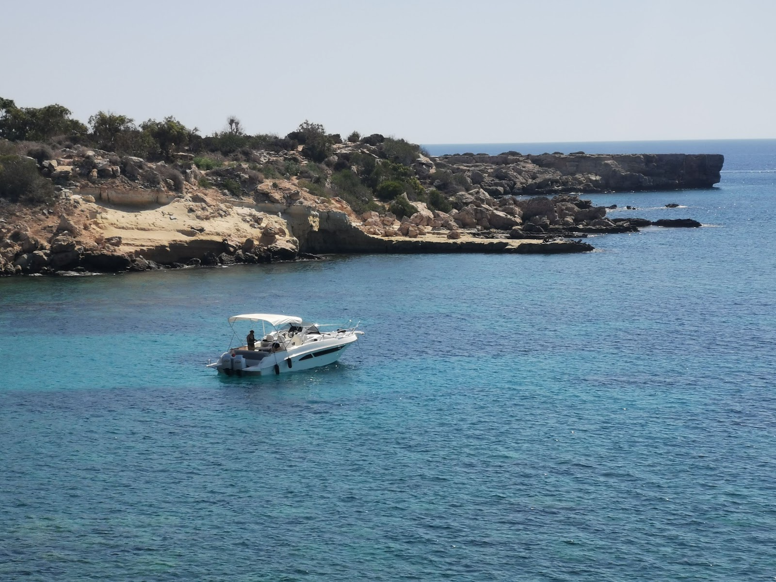 A single boat anchored in a rocky turquoise cove at Cape Greco, Ayia Napa, Cyprus